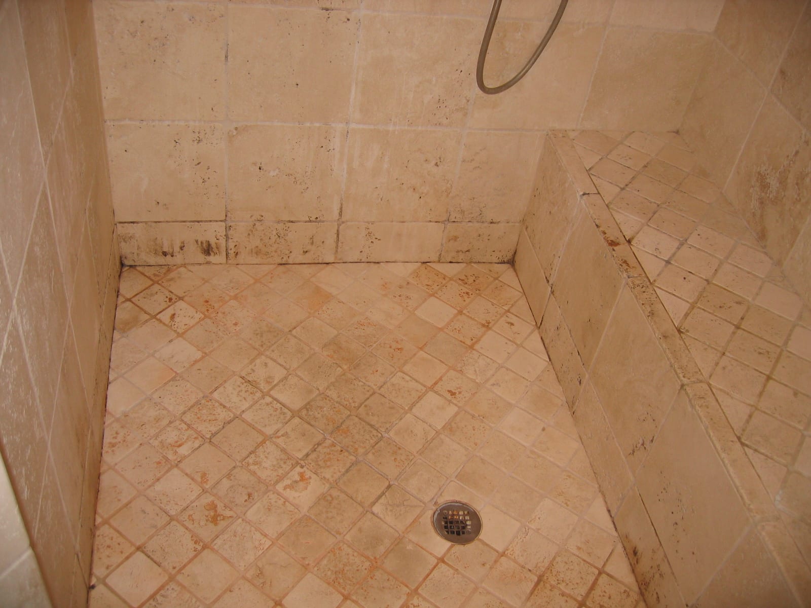 Travertine shower before: scale, soap scum and dark staining along the floor and walls